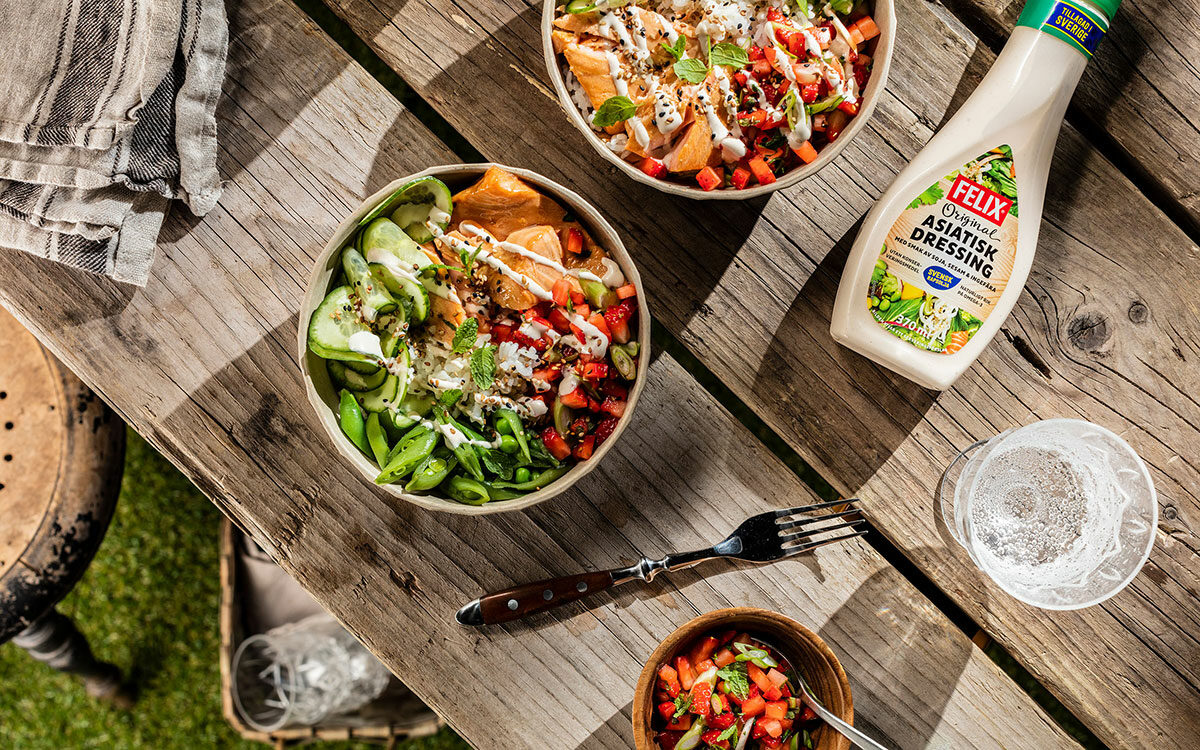 Laxbowl med grönsaker på ett somrigt bord utomhus med en flaska asiatisk dressing.